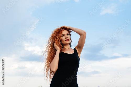 Beautiful redhead girl on the sky background