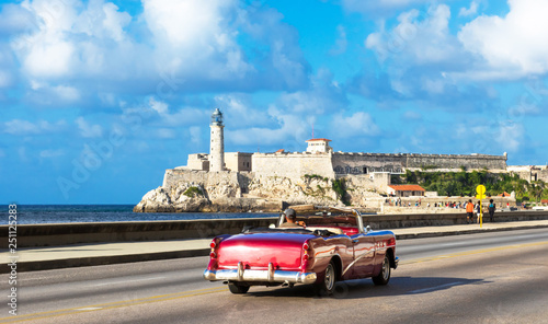 Amerikanischer purpur farbener Cabriolet Oldtimer auf dem berühmten Malecon und im Hintergrund die Festung Castillo de los Tres Reyes del Morro in Havanna Kuba - Serie Kuba Reportage photo
