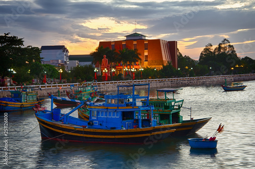 Fishing boats and ships in the town port in Phan Thiet, Binh Thuan, Vietnam, after sunset, evening colors, lanterns lit in the streets. February.