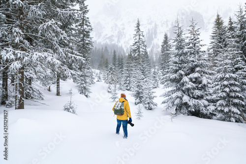 The photographer is walking in winter forest in mountains