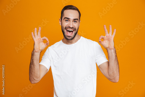 Image of joyful guy 30s with beard and mustache showing ok sign while standing, isolated over yellow background