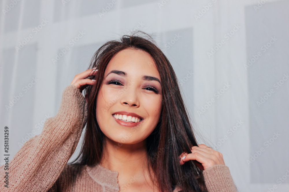 Candid portrait of sensual smiling asian girl young woman with dark long hair in cozy beige sweater, close up Candid portrait of sensual smiling asian girl young woman with dark long hair in cozy beige sweater, close up