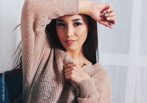 Candid portrait of sensual smiling asian girl young woman with dark long hair in cozy beige sweater sitting on blue vintage chair