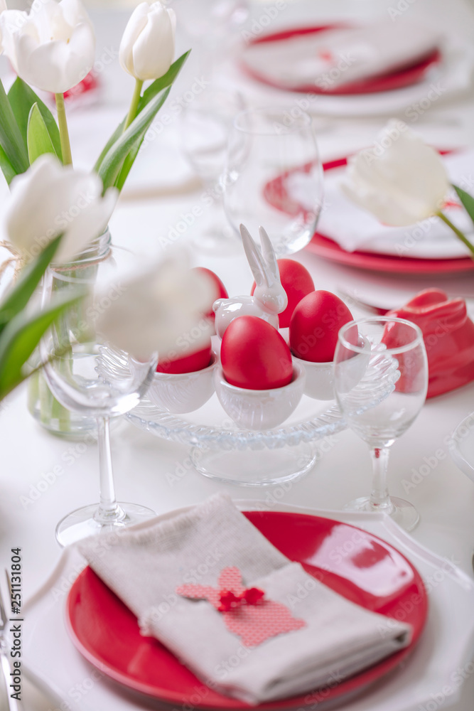 Happy easter. Decor and table setting of the Easter table is a vase with white tulips and dishes of red and white color. Easter colored eggs with white polka dots.