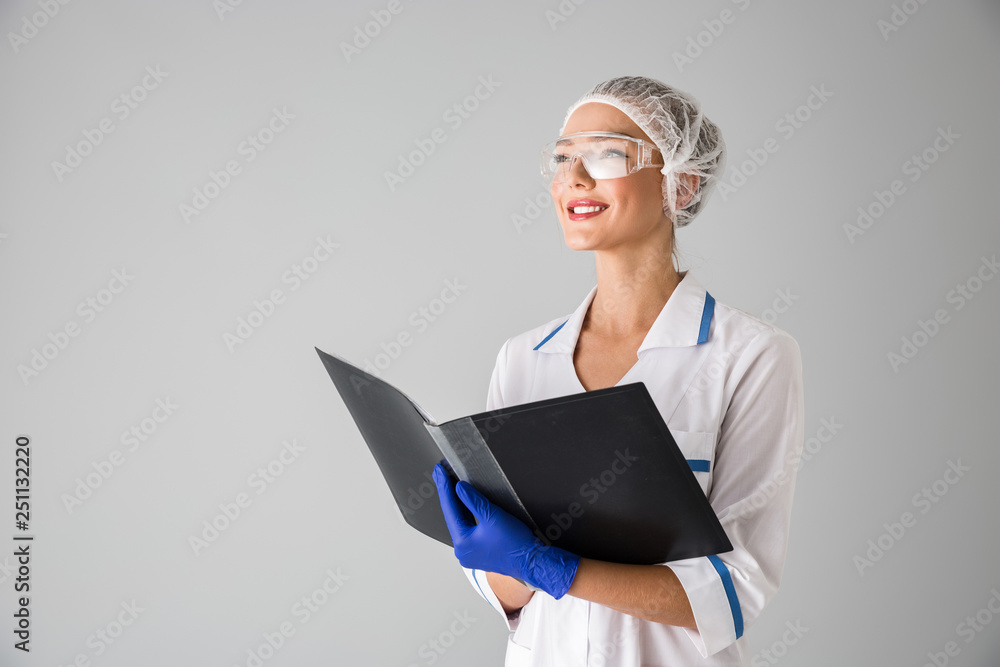 Beautiful young woman cosmetologist doctor isolated over grey wall background holding folder. Beautiful young woman cosmetologist doctor isolated over grey wall background holding folder.