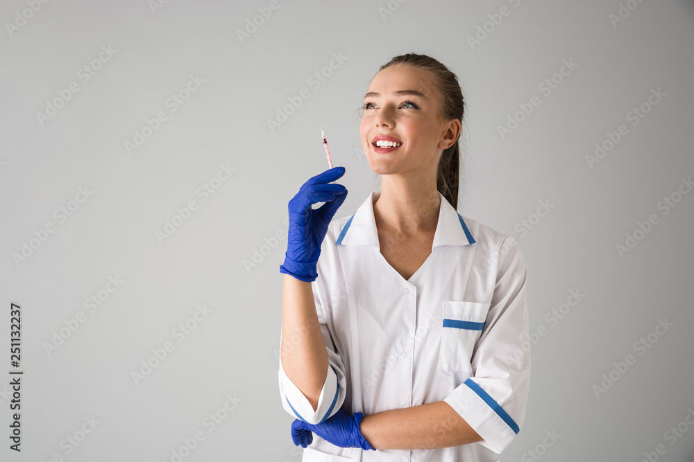 Young woman cosmetologist doctor isolated over grey wall background holding injection syringe. Young woman cosmetologist doctor isolated over grey wall background holding injection syringe.