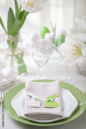 Decor and table setting of the Easter table with white tulips and dishes of green and white color. Easter decor in the form of Easter bunnies green color with white polka dots.