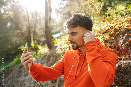 Sports fitness man runner outdoors in park listening music with earphones using mobile phone take a selfie talking.