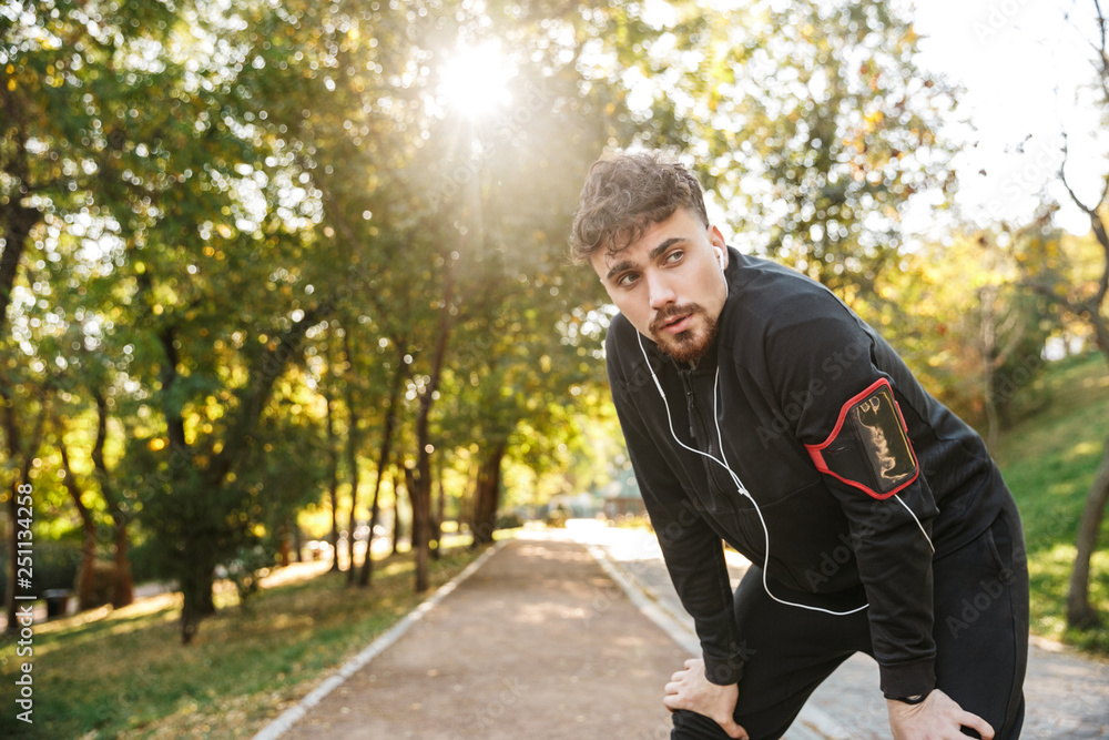 Handsome young sports fitness man runner outdoors in park listening music with earphones. Handsome young sports fitness man runner outdoors in park listening music with earphones.