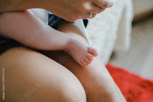 Mother holds his baby in his arms, the baby's leg.