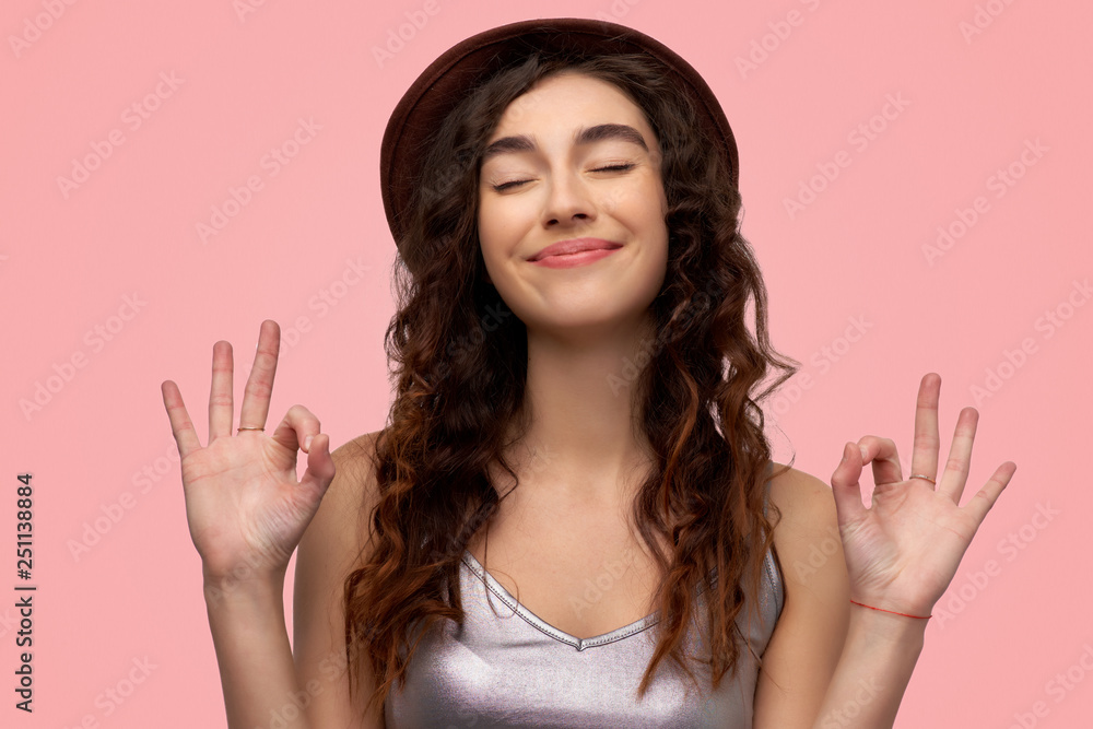 Cheerful brunette young female with glad expression, shows ok sign with both hands, dressed in casual white t shirt, demonstrates approval Cheerful brunette young female with glad expression, shows ok sign with both hands, dressed in casual white t shirt, demonstrates approval