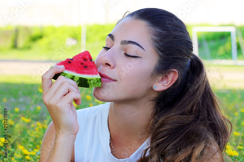 portrait of a girl with dark hair holds a juicy watermelon and enjoys, on a background of green field