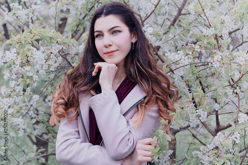 portrait of a beautiful girl with dark hair and blue eyes against the background of flowering trees, spring