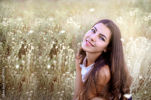 portrait of a beautiful girl with dark hair and blue eyes on the background of a blooming field