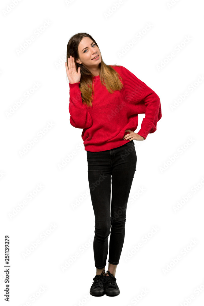 Fototapeta premium A full-length shot of a Young woman with red sweater listening to something by putting hand on the ear over isolated white background
