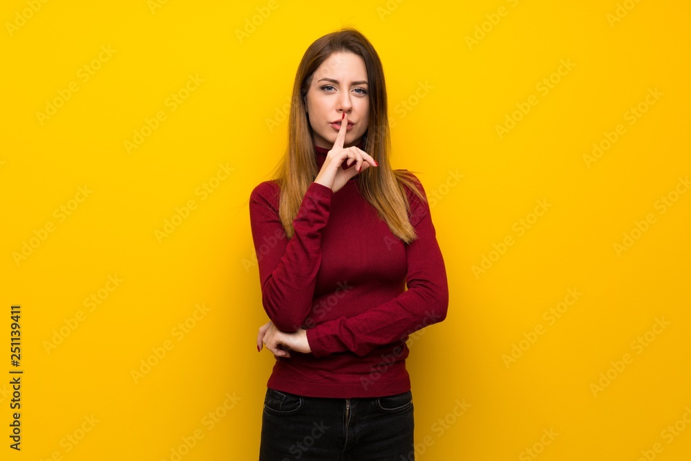 Woman with turtleneck over yellow wall showing a sign of silence gesture putting finger in mouth Woman with turtleneck over yellow wall showing a sign of silence gesture putting finger in mouth