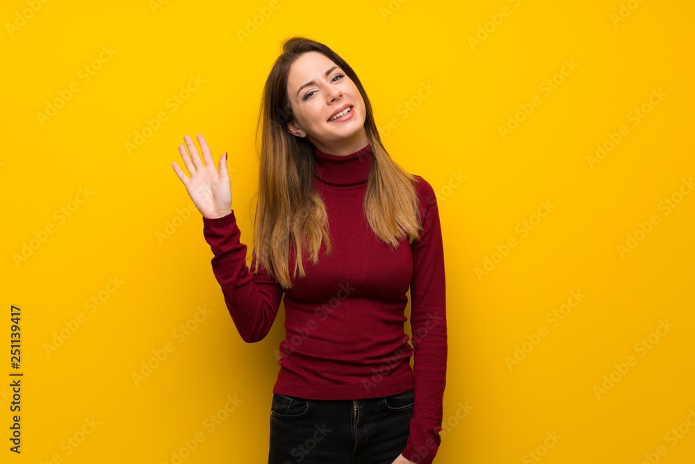 Woman with turtleneck over yellow wall saluting with hand with happy expression Woman with turtleneck over yellow wall saluting with hand with happy expression