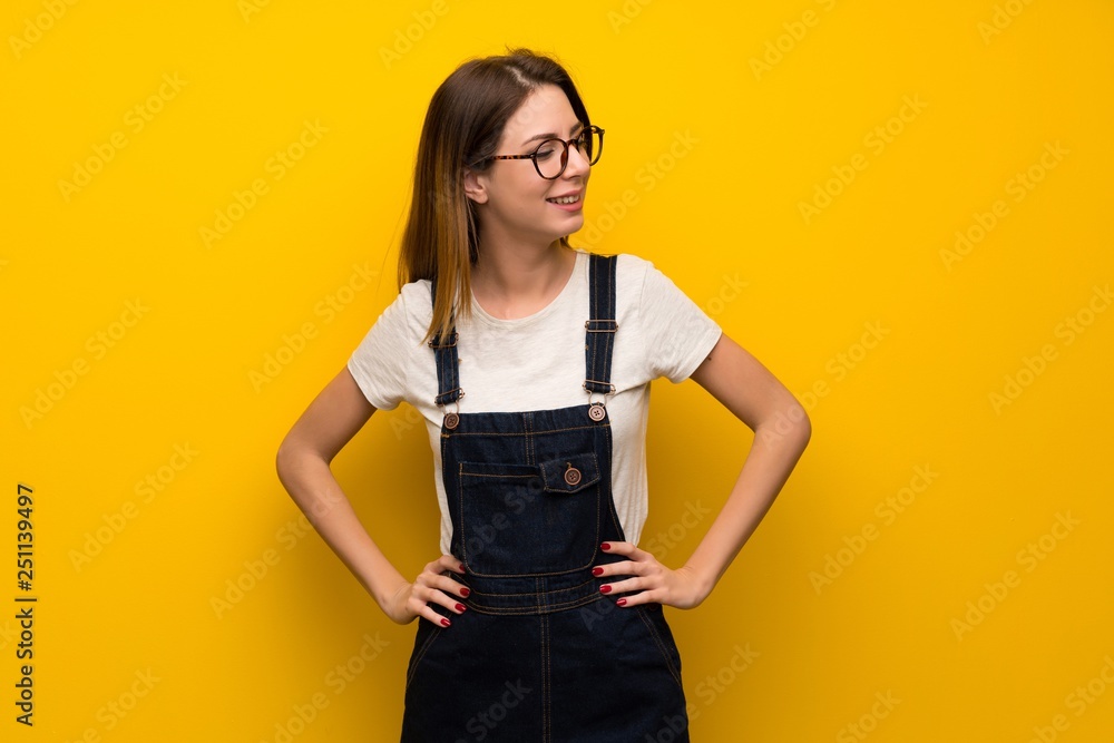 Woman over yellow wall posing with arms at hip and smiling Woman over yellow wall posing with arms at hip and smiling