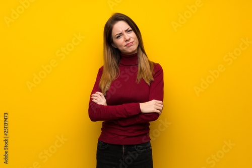 Woman with turtleneck over yellow wall feeling upset