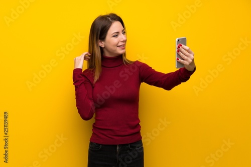 Woman with turtleneck over yellow wall making a selfie