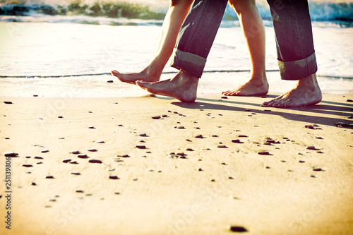 Pies descalzos de pareja paseando por la orilla de la playa al amanecer