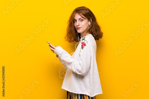 Young redhead woman over yellow wall sending a message with the mobile © luismolinero