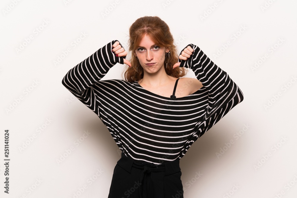Young redhead woman over white wall showing thumb down with both hands Young redhead woman over white wall showing thumb down with both hands