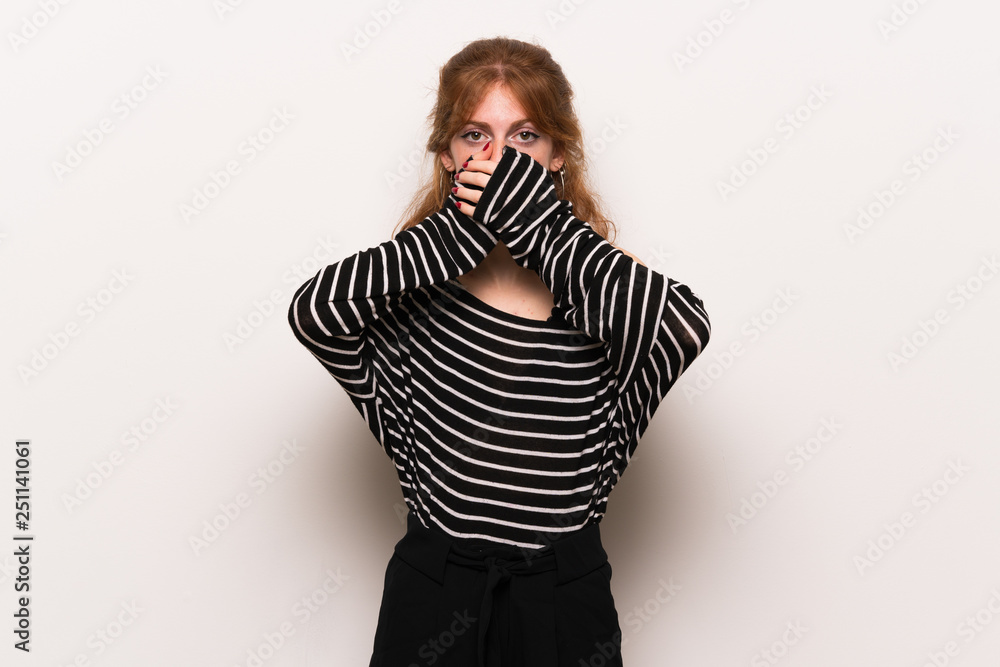 Young redhead woman over white wall covering mouth with hands for saying something inappropriate Young redhead woman over white wall covering mouth with hands for saying something inappropriate