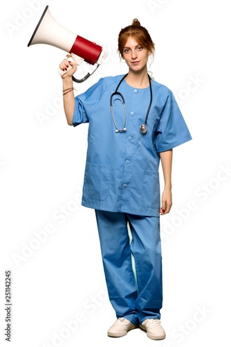 A full-length shot of a Young redhead nurse holding a megaphone over isolated white background