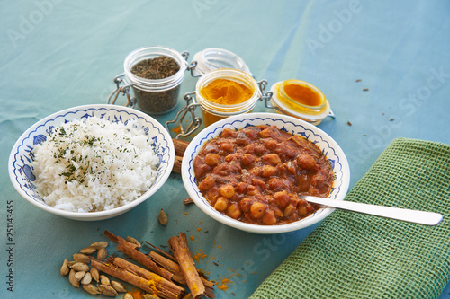 Top closeup view on hot indian vegetarian chickpea curry dish with basmati rice served in bowls,  cinnamon sticks with cardamom seeds  and curry powder in small jars. Indian vegan spicy cuisine.