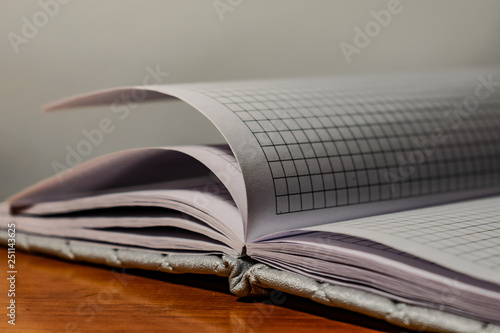 A book  a notebook with a checkered pattern on a wooden table in different poses. The cover is grey and soft with texture. Square patterns stitched with threads. Write notes in a diary. Plain white pa