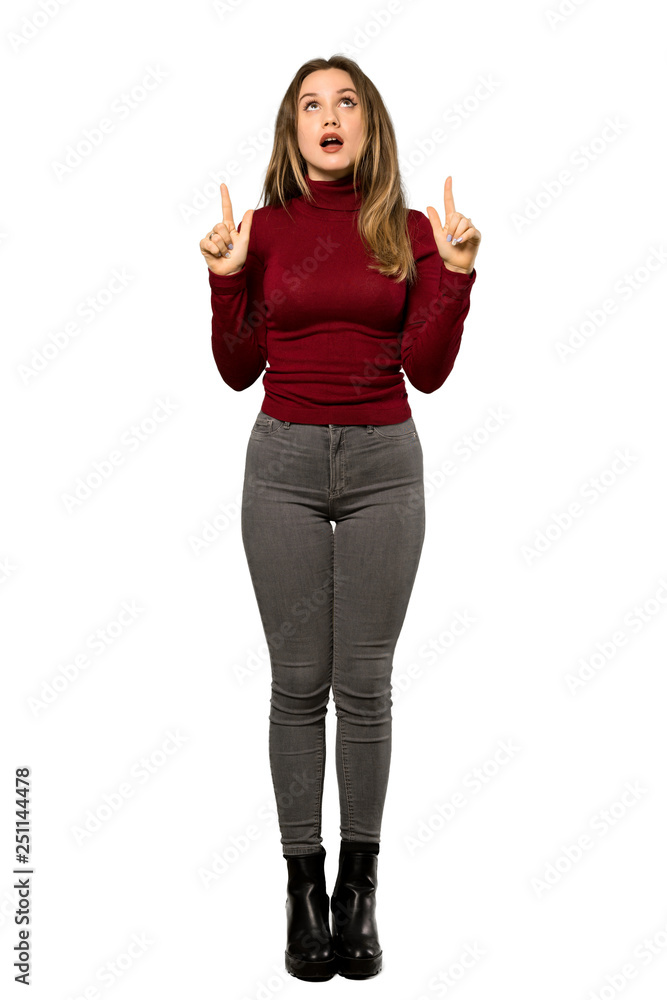 A full-length shot of a Teenager girl with turtleneck surprised and pointing up over isolated white background A full-length shot of a Teenager girl with turtleneck surprised and pointing up over isolated white background