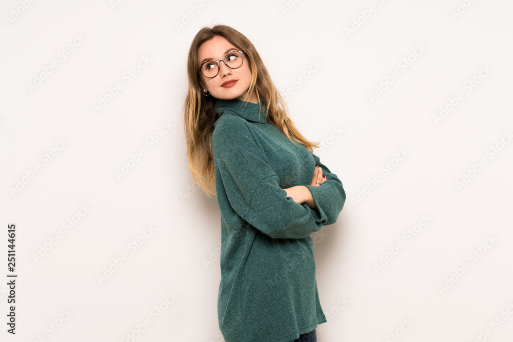 Teenager girl over white wall looking over the shoulder with a smile Teenager girl over white wall looking over the shoulder with a smile