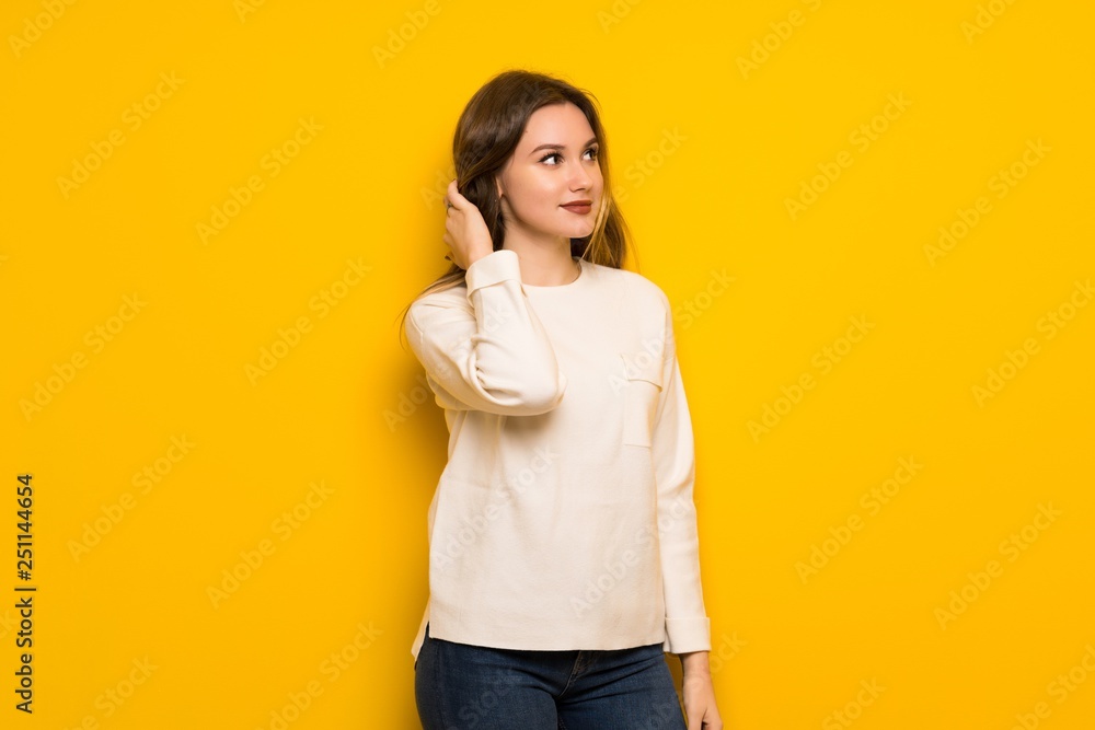 Teenager girl over yellow wall thinking an idea while scratching head Teenager girl over yellow wall thinking an idea while scratching head