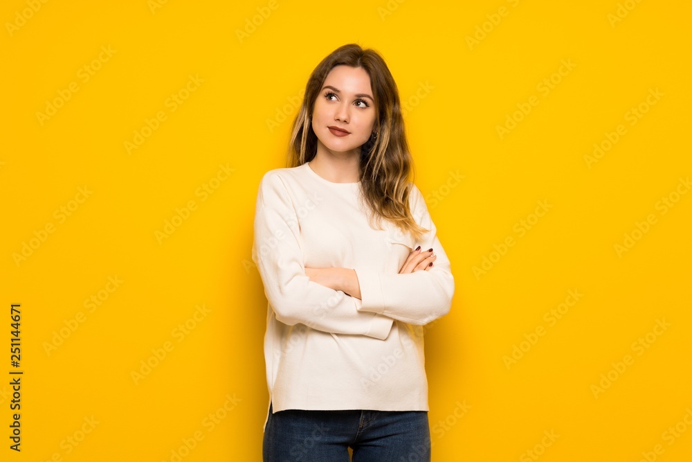 Teenager girl over yellow wall looking up while smiling Teenager girl over yellow wall looking up while smiling