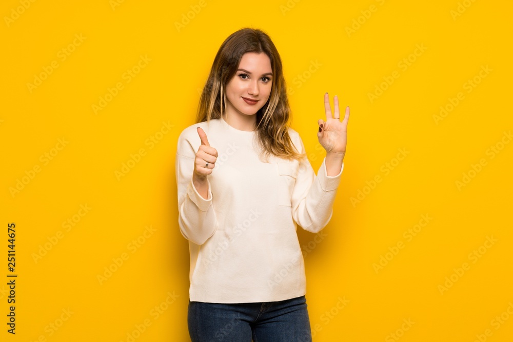 Teenager girl over yellow wall showing ok sign with and giving a thumb up gesture Teenager girl over yellow wall showing ok sign with and giving a thumb up gesture