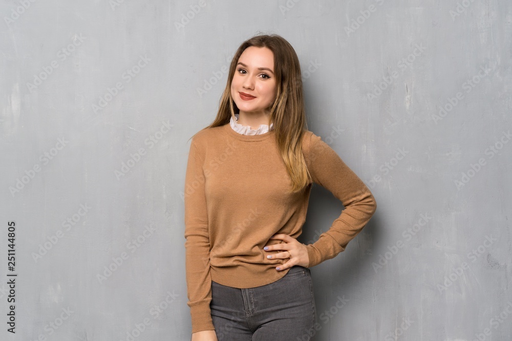 Teenager girl over textured wall posing with arms at hip and smiling Teenager girl over textured wall posing with arms at hip and smiling