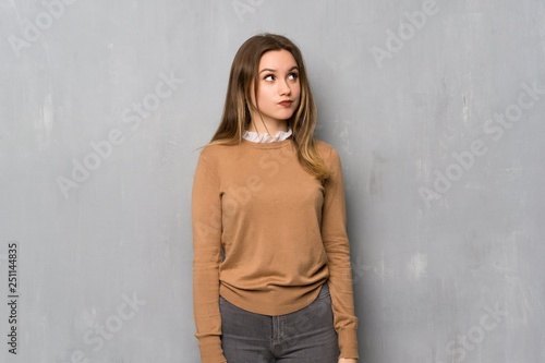 Teenager girl over textured wall with confuse face expression while bites lip © luismolinero