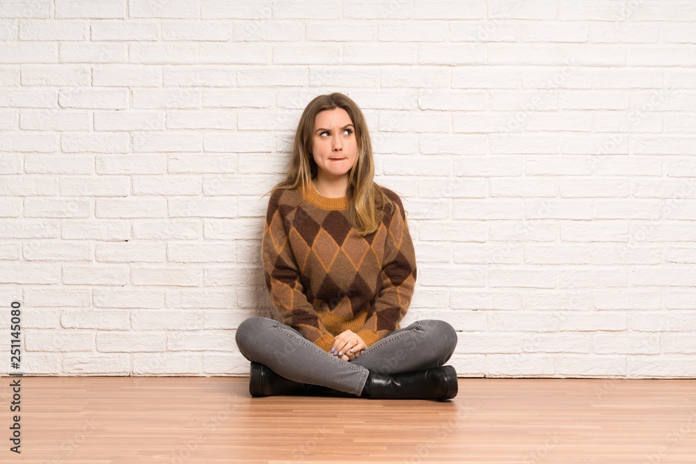 Teenager girl sitting on the floor with confuse face expression while bites lip Teenager girl sitting on the floor with confuse face expression while bites lip