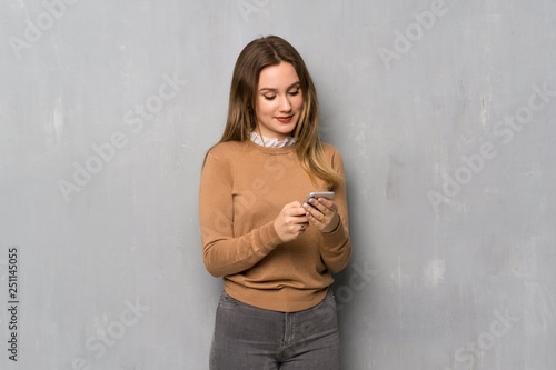 Teenager girl over textured wall sending a message with the mobile