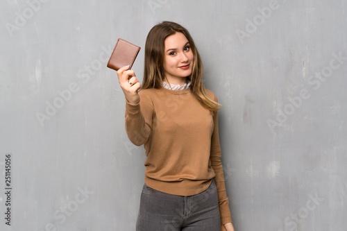 Teenager girl over textured wall holding a wallet