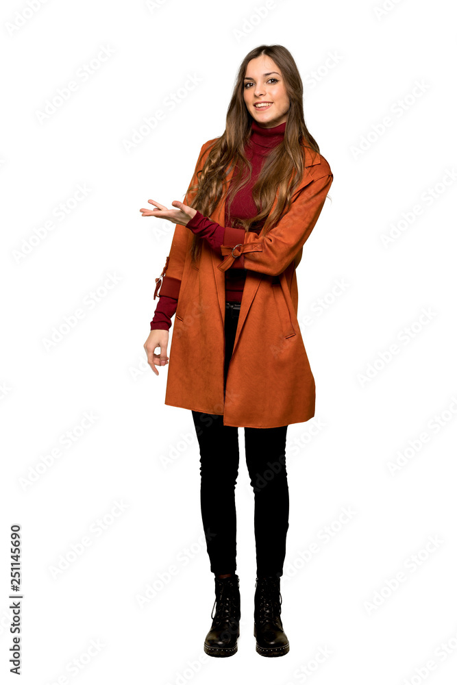 Full-length shot of Young woman with coat presenting an idea while looking smiling towards on isolated white background