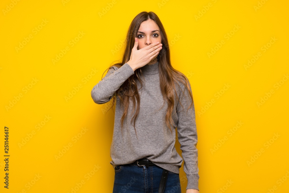 Young woman over yellow wall covering mouth with hands for saying something inappropriate Young woman over yellow wall covering mouth with hands for saying something inappropriate