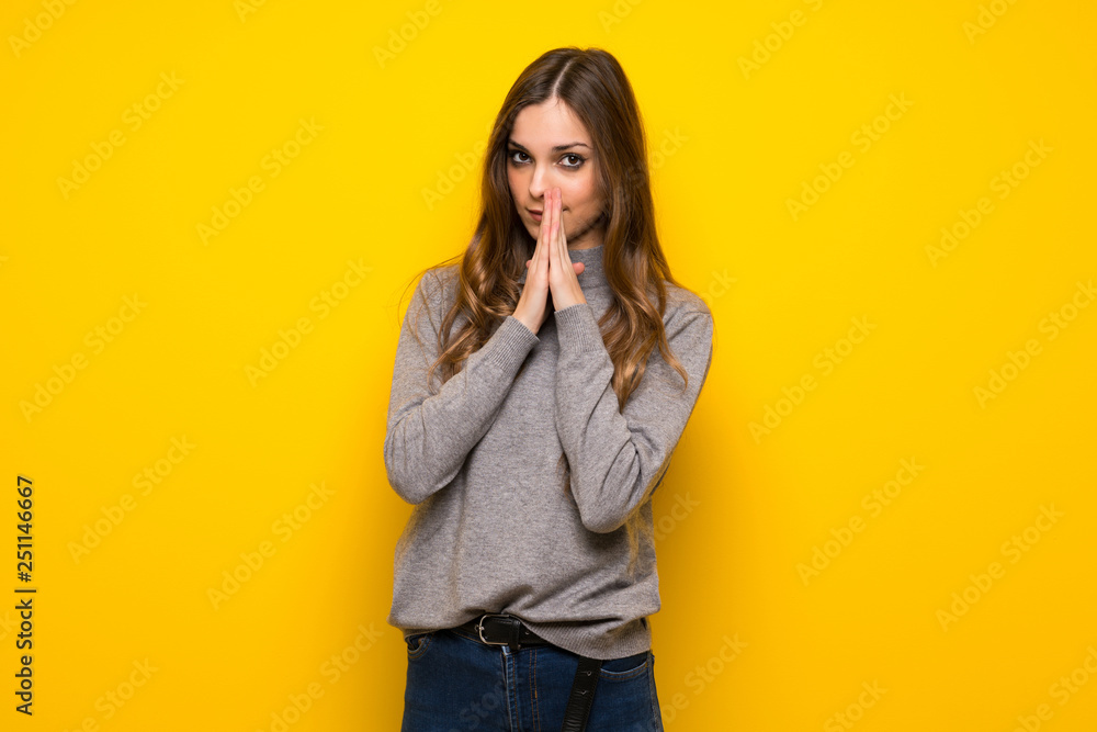 Young woman over yellow wall keeps palm together. Person asks for something Young woman over yellow wall keeps palm together. Person asks for something