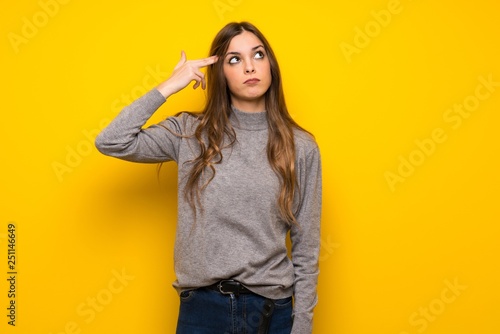 Young woman over yellow wall with problems making suicide gesture