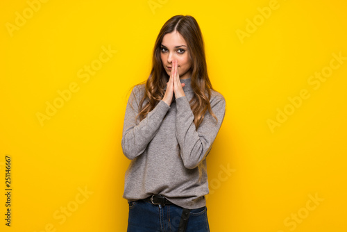 Young woman over yellow wall keeps palm together. Person asks for something