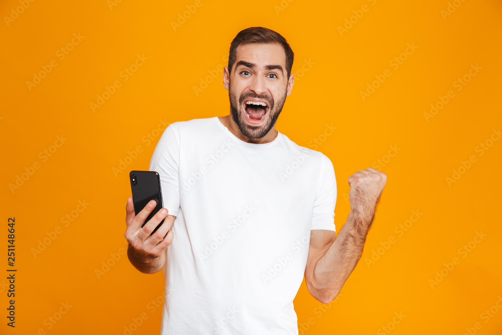Photo of brunette man 30s in casual wear screaming and holding smartphone, isolated over yellow background Photo of brunette man 30s in casual wear screaming and holding smartphone, isolated over yellow background
