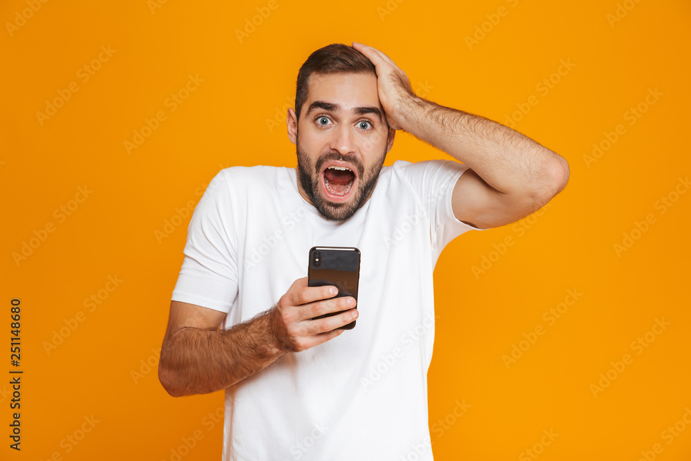 Photo of excited man 30s in casual wear smiling and holding smartphone, isolated over yellow background Photo of excited man 30s in casual wear smiling and holding smartphone, isolated over yellow background