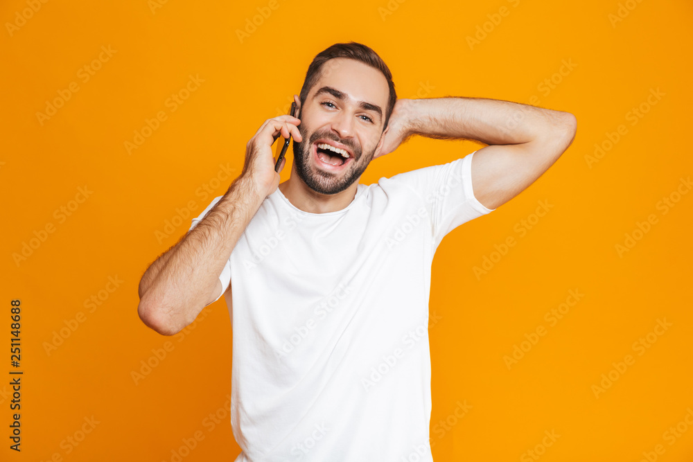 Photo of attractive man 30s in casual wear smiling and talking on mobile phone, isolated over yellow background Photo of attractive man 30s in casual wear smiling and talking on mobile phone, isolated over yellow background