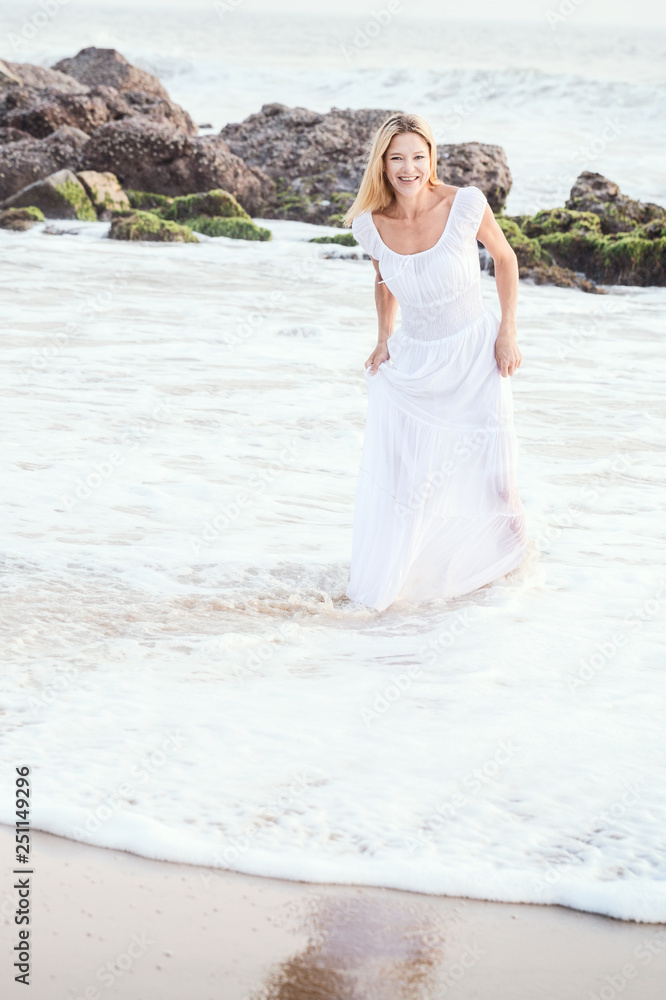 Attractive happy mature tourist blonde woman in long white dress on asian sand tropical beach. Attractive happy mature tourist blonde woman in long white dress on asian sand tropical beach.